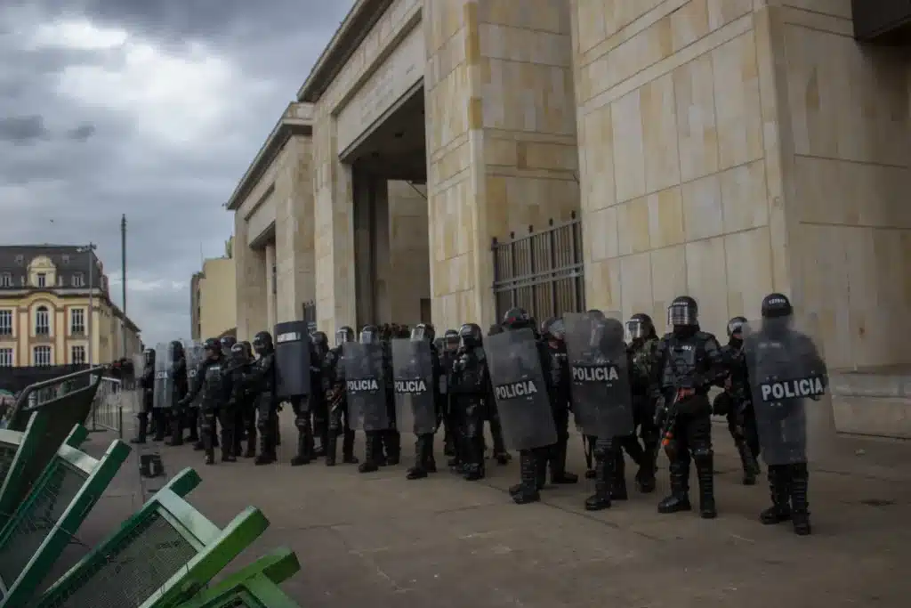 Policiais usando escudos e equipamentos de proteção durante confronto em via pública.