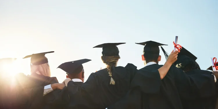 Grupo de formandos comemorando a graduação ao ar livre, simbolizando o momento de transição entre a conquista acadêmica e as dificuldades profissionais.
