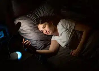 Pessoa deitada na cama usando o celular durante a madrugada, ilustrando os efeitos de dormir tarde no organismo.