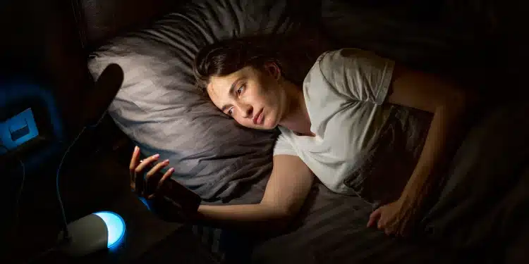 Pessoa deitada na cama usando o celular durante a madrugada, ilustrando os efeitos de dormir tarde no organismo.