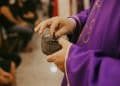 Sacerdote aplicando cinzas em pessoa na Quarta-feira de Cinzas, tradição religiosa da Igreja Católica.