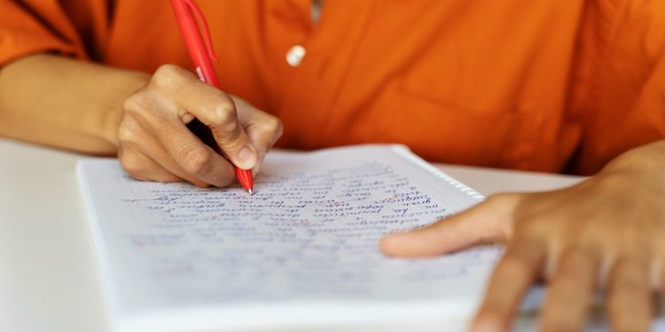 Pessoa escrevendo com caneta vermelha em caderno quadriculado representando candidato estudando os salários e benefícios do concurso SAMAE Campos Novos SC