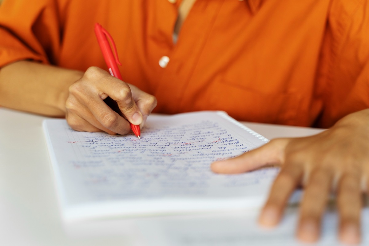 Pessoa escrevendo com caneta vermelha em caderno quadriculado representando candidato estudando os salários e benefícios do concurso SAMAE Campos Novos SC
