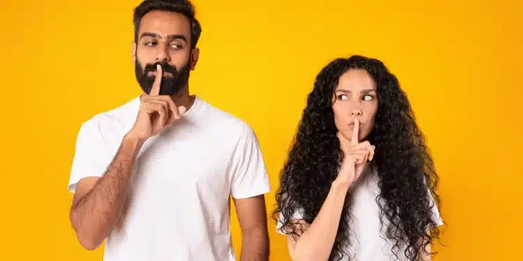 Homem e mulher fazendo gesto de silêncio com o dedo nos lábios, representando a importância de manter informações pessoais em sigilo.