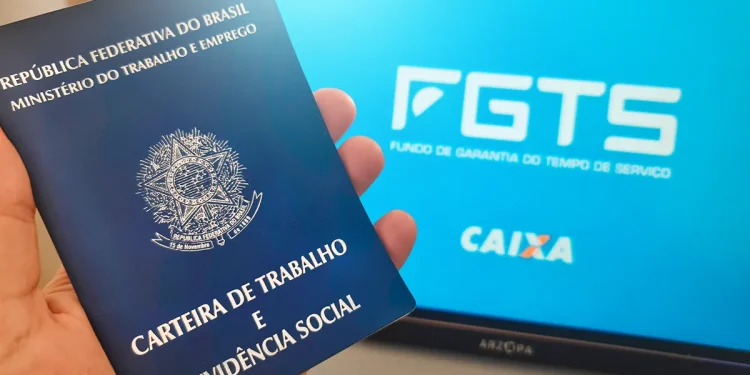 Mão segurando carteira de trabalho azul em frente a monitor exibindo logo do FGTS e Caixa