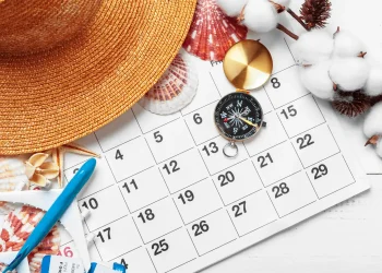 Calendário com chapéu de verão, bússola e miniatura de avião representando planejamento do feriado da Sexta-feira da Paixão 2026.