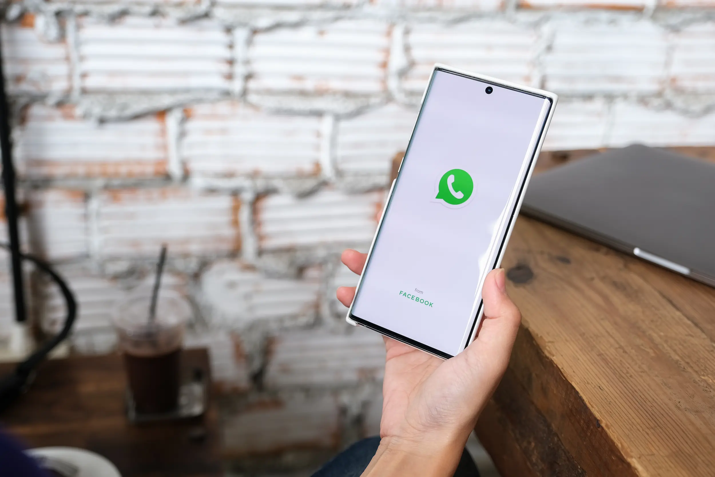 Pessoa segurando um smartphone com o logo do WhatsApp na tela.