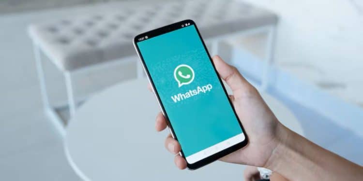 Pessoa segurando um smartphone com a tela do WhatsApp visível, mostrando o ícone do aplicativo em um ambiente moderno e claro.