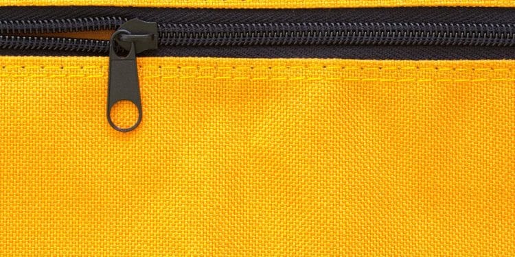 Close-up macro de um zíper preto com cursor metálico fechado em um tecido de lona amarela vibrante com costura visível.