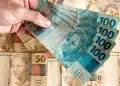Dinheiro em notas de 100 e 50 reais nas mãos de uma pessoa, representando o pagamento ou antecipação do 13º salário do INSS.