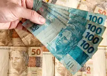 Dinheiro em notas de 100 e 50 reais nas mãos de uma pessoa, representando o pagamento ou antecipação do 13º salário do INSS.