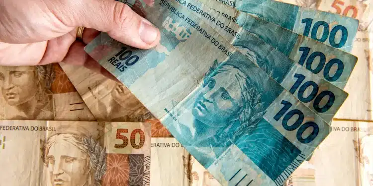 Dinheiro em notas de 100 e 50 reais nas mãos de uma pessoa, representando o pagamento ou antecipação do 13º salário do INSS.