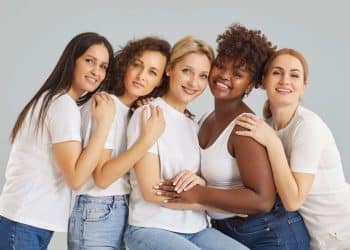 Grupo de mulheres de diferentes origens unidas e sorrindo, representando a luta por igualdade de direitos celebrada no Dia Internacional da Mulher em 8 de março.