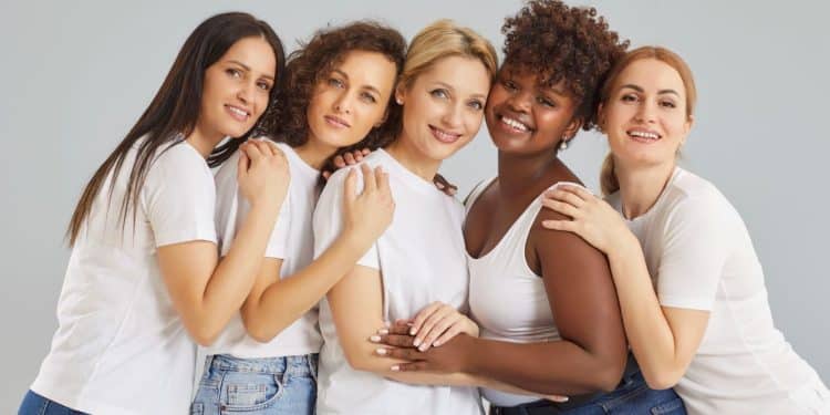Grupo de mulheres de diferentes origens unidas e sorrindo, representando a luta por igualdade de direitos celebrada no Dia Internacional da Mulher em 8 de março.