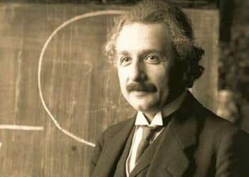 Albert Einstein diante de um quadro com fórmulas, físico conhecido pela teoria da relatividade e por reflexões sobre o sentido da felicidade.
