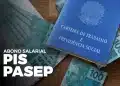 Carteira de trabalho azul sobre notas de R$ 100 distribuídas em mesa de madeira