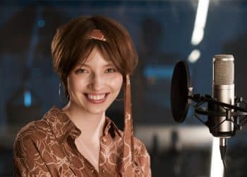 Atriz sorrindo diante de microfone profissional em estúdio moderno iluminado, simbolizando as profissões extintas.