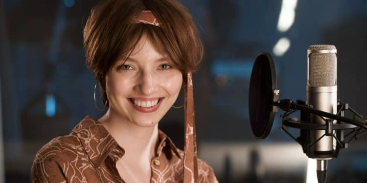 Atriz sorrindo diante de microfone profissional em estúdio moderno iluminado, simbolizando as profissões extintas.