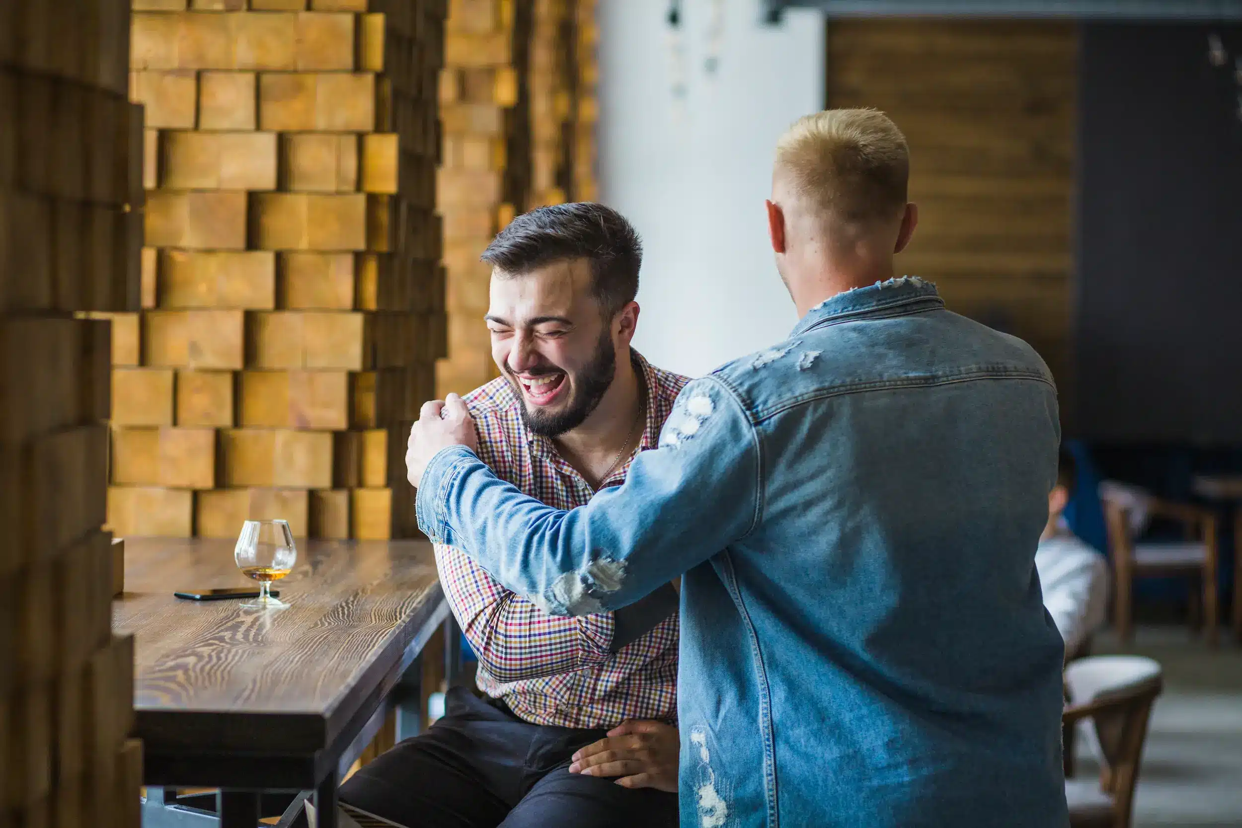 Dois amigos rindo e conversando em um bar, demonstrando conexão positiva e reconhecimento do outro em uma conversa.