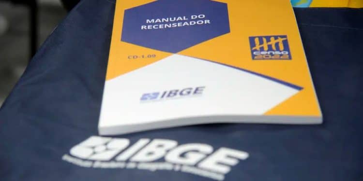 Manual do recenseador do IBGE sobre mesa, ilustrando materiais usados nas pesquisas de campo e preparação para o concurso de 2026.