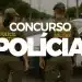 Um casal de policiais militares (mulher e homem), vistos de costas, em uniforme verde-oliva, parados em uma rua de cidade. Ao lado deles, uma viatura policial branca com giroflex ligado. O texto 'CONCURSO POLÍCIA' em branco está sobreposto no centro da imagem.