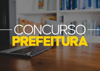 Notebook ligado sobre mesa de madeira com estante de livros ao fundo e texto "Concurso Prefeitura" em destaque.