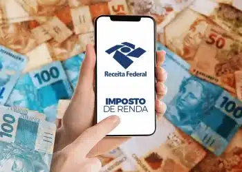 Celular exibindo aplicativo do Imposto de Renda da Receita Federal sobre notas de real ao fundo.