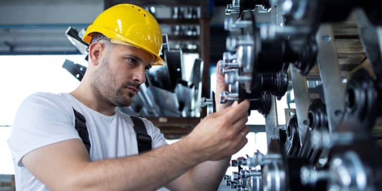 Operário usando capacete amarelo ajusta engrenagens em equipamento industrial.