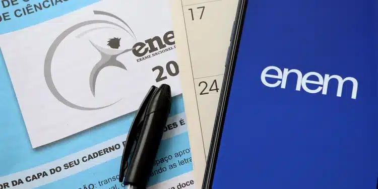 Foto de material do Enem com caderno de prova, caneta e celular exibindo o aplicativo oficial do exame.