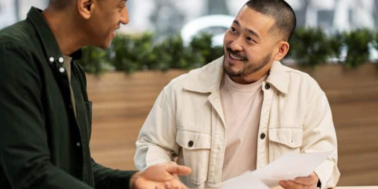 Dois homens conversando em uma mesa enquanto analisam documentos, demonstrando escuta ativa e respeito durante o diálogo.