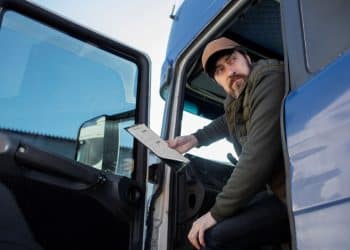 Homem sentado em um caminhão, segurando um documento, representando os caminhoneiros na greve.