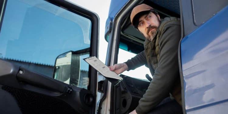 Homem sentado em um caminhão, segurando um documento, representando os caminhoneiros na greve.