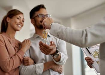 Corretor entregando as chaves de um imóvel para um casal durante negociação imobiliária.