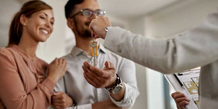 Corretor entregando as chaves de um imóvel para um casal durante negociação imobiliária.