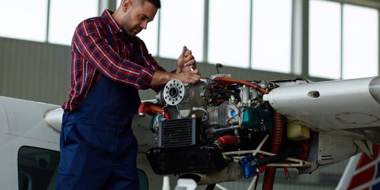 Técnico de manutenção aeronáutica realizando ajustes no motor de um pequeno avião dentro de um hangar.