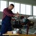 Técnico de manutenção aeronáutica realizando ajustes no motor de um pequeno avião dentro de um hangar.