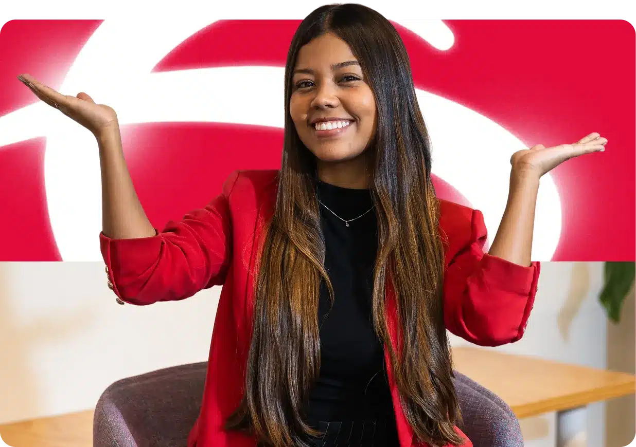 Jovem sentada com blazer vermelho, sorrindo e levantando as mãos em ambiente corporativo.