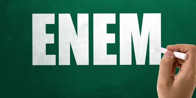 Mão escrevendo a palavra ENEM no quadro verde com giz branco, simbolizando o Exame Nacional do Ensino Médio.