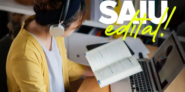 Mulher com fone de ouvido estuda com livro aberto e anotações ao lado de notebook.