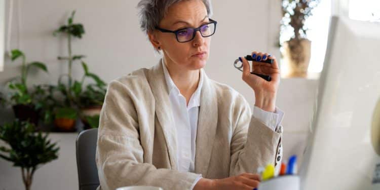 Profissional com mais de 50 anos trabalhando como autônoma no computador em escritório doméstico.