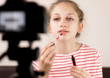 Menina aplicando maquiagem enquanto é filmada, refletindo a adultização infantil e seus riscos no desenvolvimento.