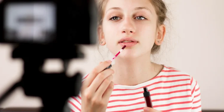 Menina aplicando maquiagem enquanto é filmada, refletindo a adultização infantil e seus riscos no desenvolvimento.