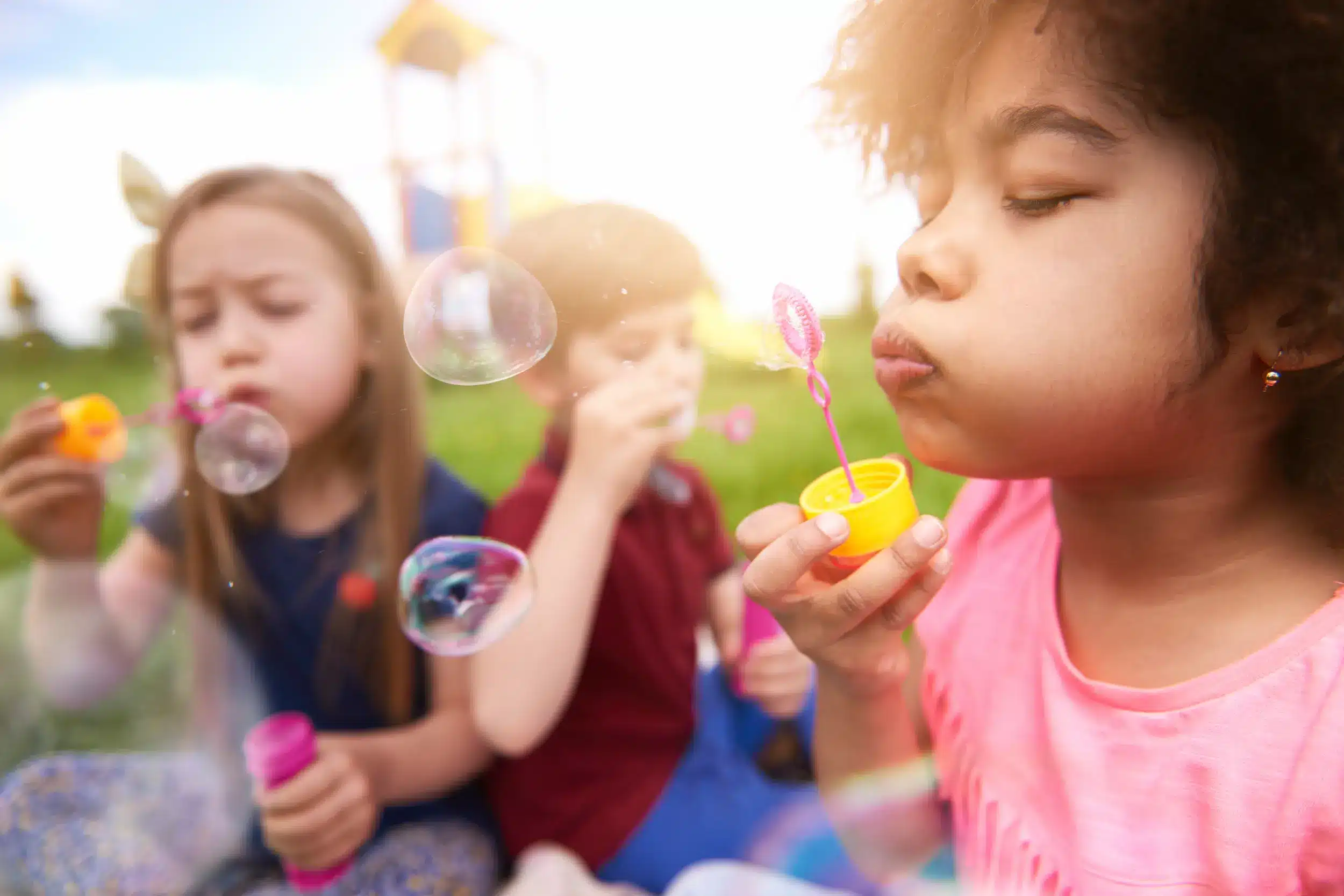 Crianças brincando com bolhas de sabão ao ar livre, um momento de diversão e interação essencial para o desenvolvimento infantil.