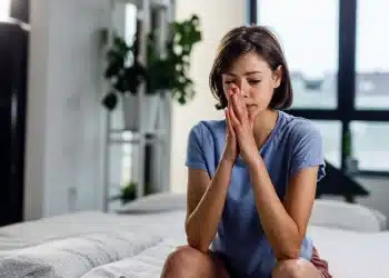 Pessoa com expressão de ansiedade sentada na cama, simbolizando o sentimento de apreensão que atinge muitas pessoas nas noites de domingo.