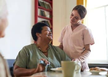 Mulher assistente de saúde cuidando de paciente em lar de idosos, destacando o papel das mulheres em profissões com salários mais altos do que os homens.