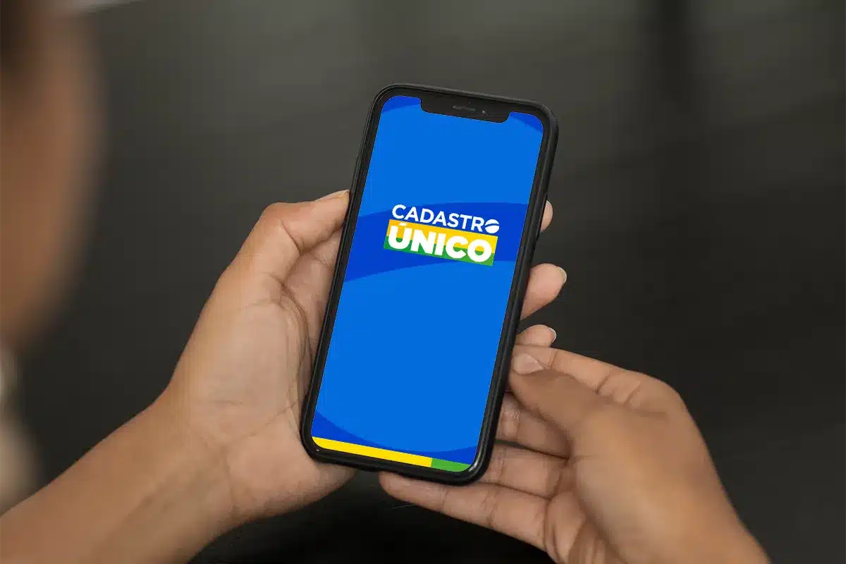 Mãos segurando celular com o aplicativo do CadÚnico aberto, mostrando como verificar e atualizar o cadastro pelo smartphone para não perder benefícios sociais