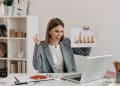 Mulher de negócios comemorando bons resultados de produtividade, segurando gráfico durante videoconferência.