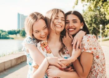 Três amigas sorridentes se abraçando ao ar livre em um dia ensolarado, transmitindo afeto e bem-estar.