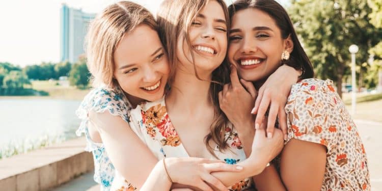 Três amigas sorridentes se abraçando ao ar livre em um dia ensolarado, transmitindo afeto e bem-estar.