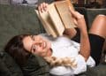 Mulher sorridente deitada no sofá lendo um livro — como transformar a leitura em hábito com passo a passo fácil para quem vive ocupado
